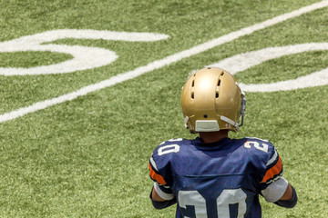 Kid standing back on a football field with gold helmet and blue jersey 