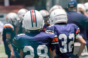 Kid standing back on a football field with white helmet and blue jersey watching other kids play  