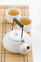 teapot and cups of green tea on a wicker mat