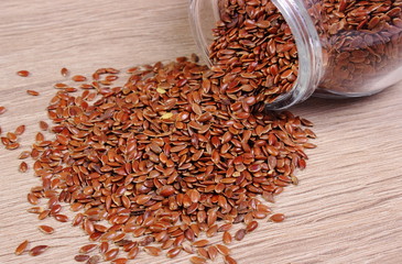 Linseed spilling out of jar on wooden background