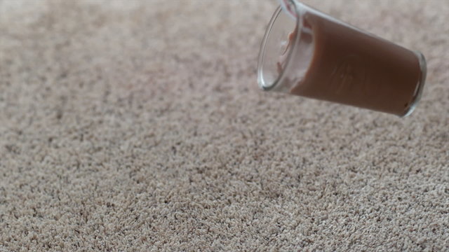 Glass of chocolate milk spilling on carpet in slow motion