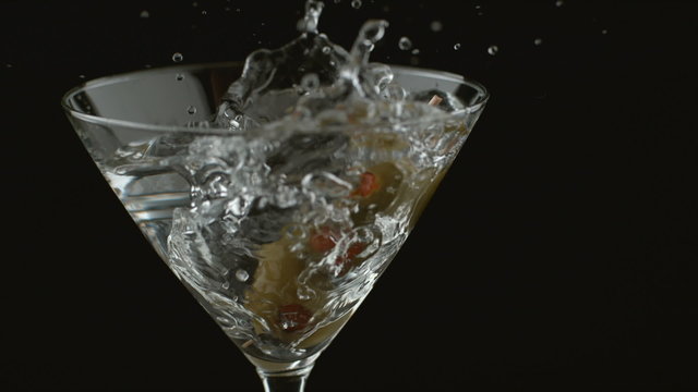 Slow motion shot of olives splashing into martini