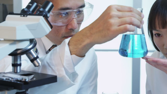 Scientists in lab looking at beaker of liquid