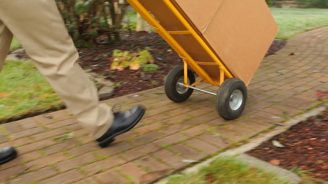 Delivery man pushes dolly full of packages to home