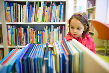 Little girl is choosing a book in the library