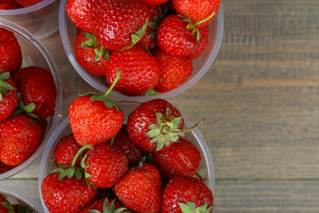 Fresh strawberries in a plastic bowl on wooden background