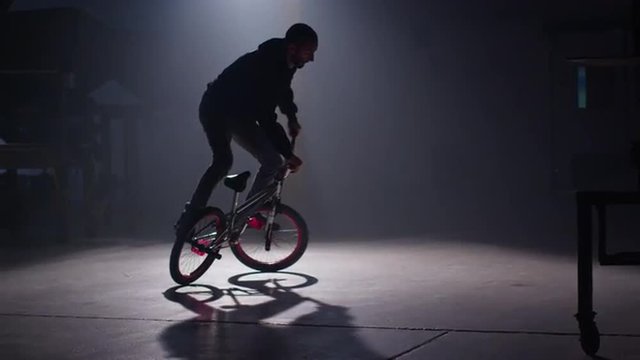 BMX rider doing tricks in dark warehouse.