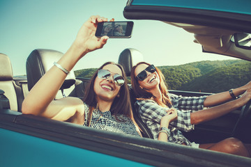Two attractive young women dtaking selfe in a convertible car
