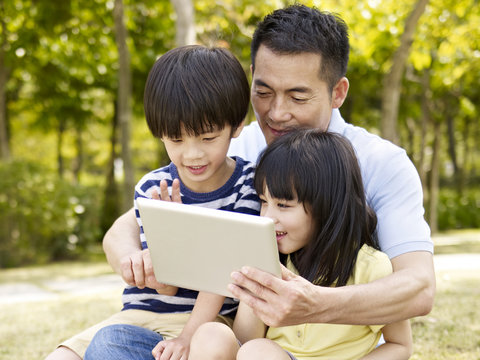 asian father and children using tablet outdoors