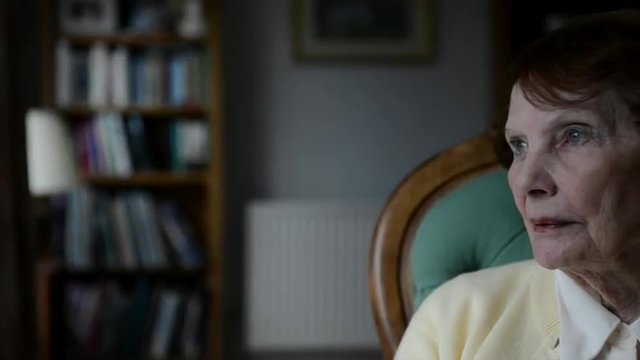 Pan left to right of Elderly woman sitting in chair gazing out of window