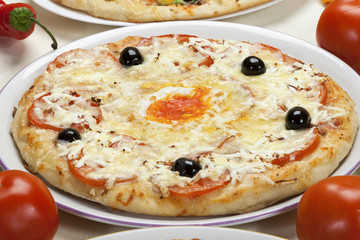 Pizza with cheese, tomato and egg served on a plate.
