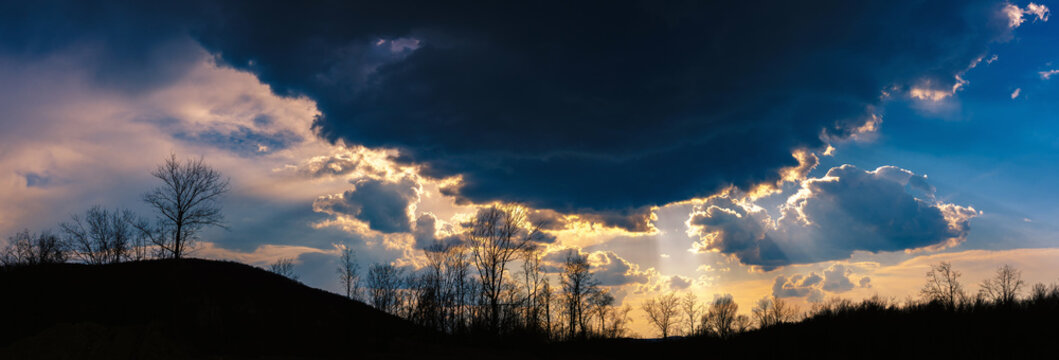 Panorama of a early spring landscape in the evening before storm with sun beams from dark gloomy clouds