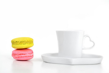 Colorful macarons with coffee in white cup and plate on white ba
