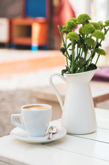 cup of cappuccino on table with white vase