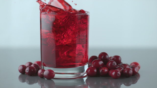 Ice splashing into cranberry juice in slow motion