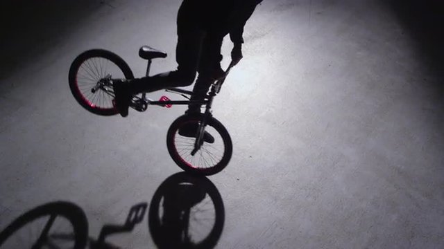 BMX rider doing tricks in dark warehouse.