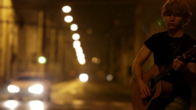 Young rocker guitarist on the night traffic street