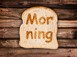 Text Morning toasted on a slice of bread, isolated on wood background © Delphotostock