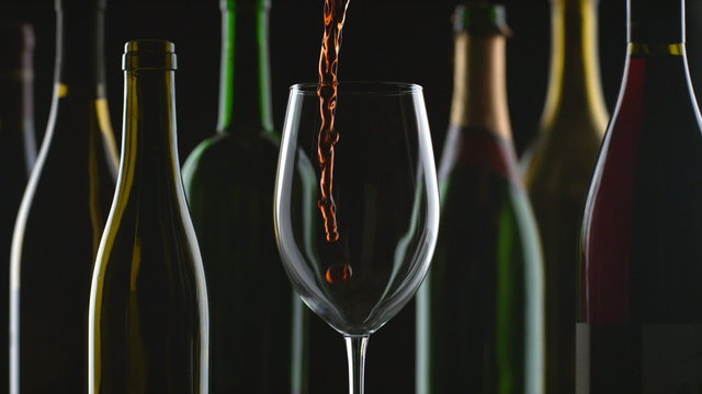 Slow motion shot of red wine pouring with bottles and black background