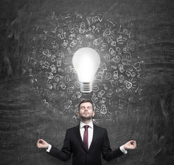 Meditating young businessman thinking about the light bulb. A concept of the brainstorm in business development.