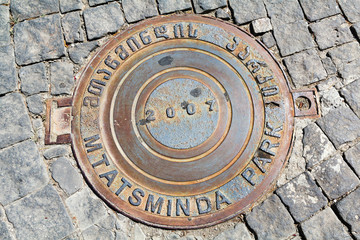 Round steel sewer manhole on the cobblestone road 