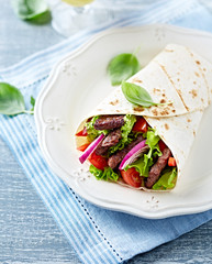 A fajita filled with grilled pork and fresh vegetables