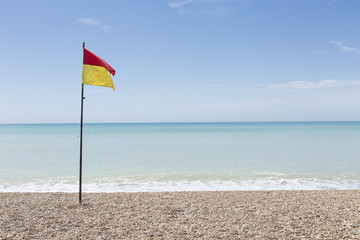 Lifeguard flag on a pebbly beach on a bright sunny day