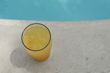 Glass of orange juice with ice cubes by the swimming pool