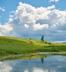 Obraz premium Reflection of the sky with clouds in the water near the green hill