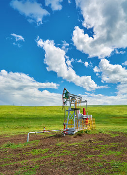 Pumping unit for pumping oil on a green meadow against a blue sky with clouds in summer