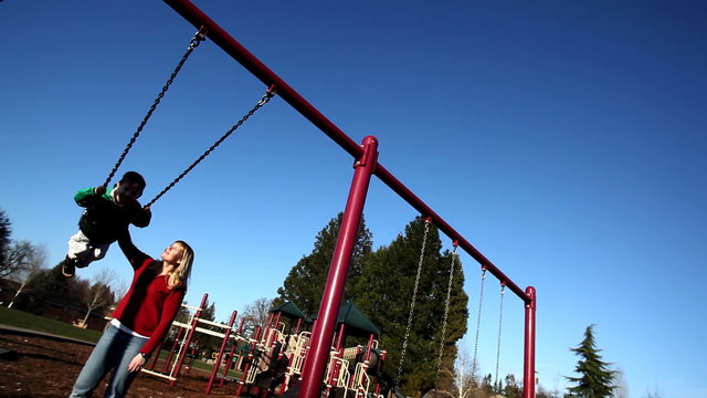 Mother pushing young boy on swing