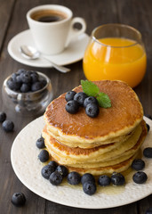 Pancakes with fresh blueberries and honey on wooden table