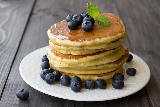 Pancakes with fresh blueberries and honey on wooden table