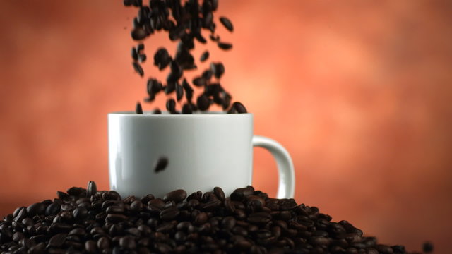 Coffee beans falling into coffee mug, slow motion