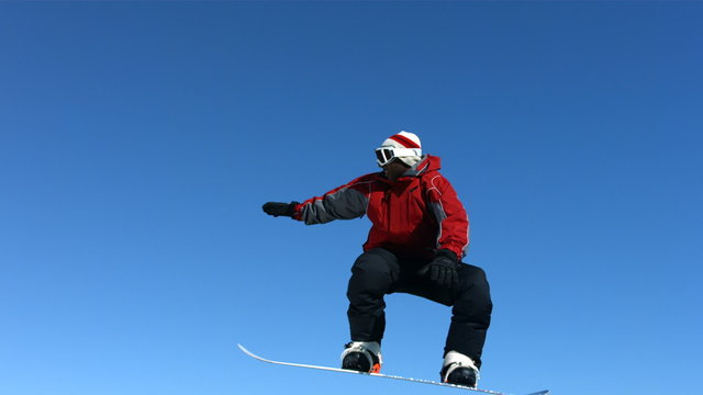 Snowboarder jumps into air and grabs board, slow motion