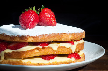 A homemade Swedish strawberry layer cake filled with fresh strawberries and a custard cream. Topped with fresh strawberries and dusted with icing sugar.