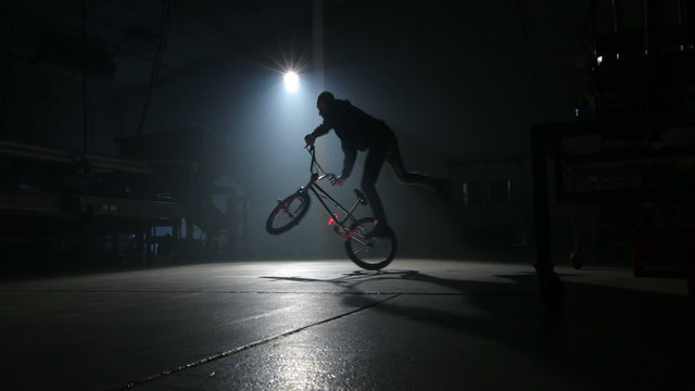 BMX rider doing tricks in dark warehouse