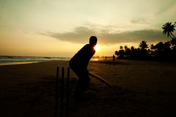 Boy playing cricket at sunset on tropical beach in Sri Lanka