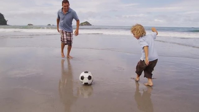 Father and son kicking soccer ball together at beach