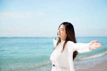 Asian woman enjoying beach, close eyes and open arms