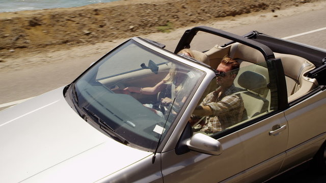 Couple driving convertible together along beach