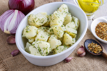 Bowl of boiled potatoes, fresh vegetables and herbs around