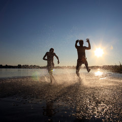 Glückliche junge Menschen laufen und springen am See beim Sonnenuntergang