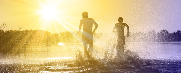 Glückliche junge Menschen laufen und springen am See beim Sonnenuntergang