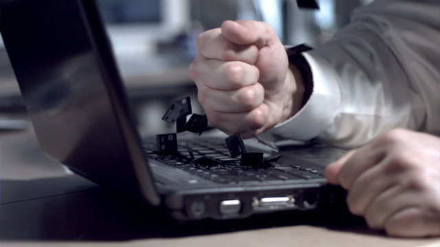 Businessman smashing laptop with fist, slow motion