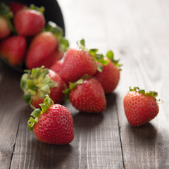 Fresh red strawberries in an aluminum bowl on wooden background.