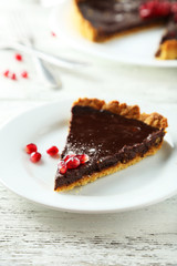 Homemade chocolate tart with pomegranate on white wooden background