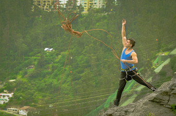 athletic man standing on cliff throwing rope down mountain