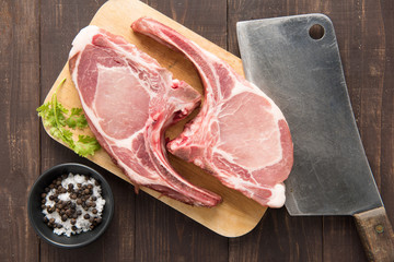 Raw pork chop steak on cutting board and cleaver on wooden backg
