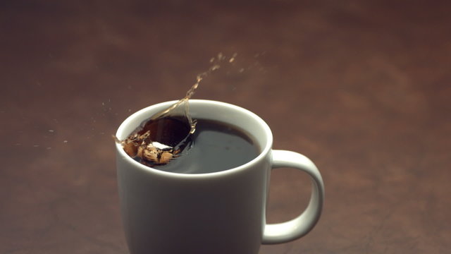 Sugar cubes splashing into coffee cup
